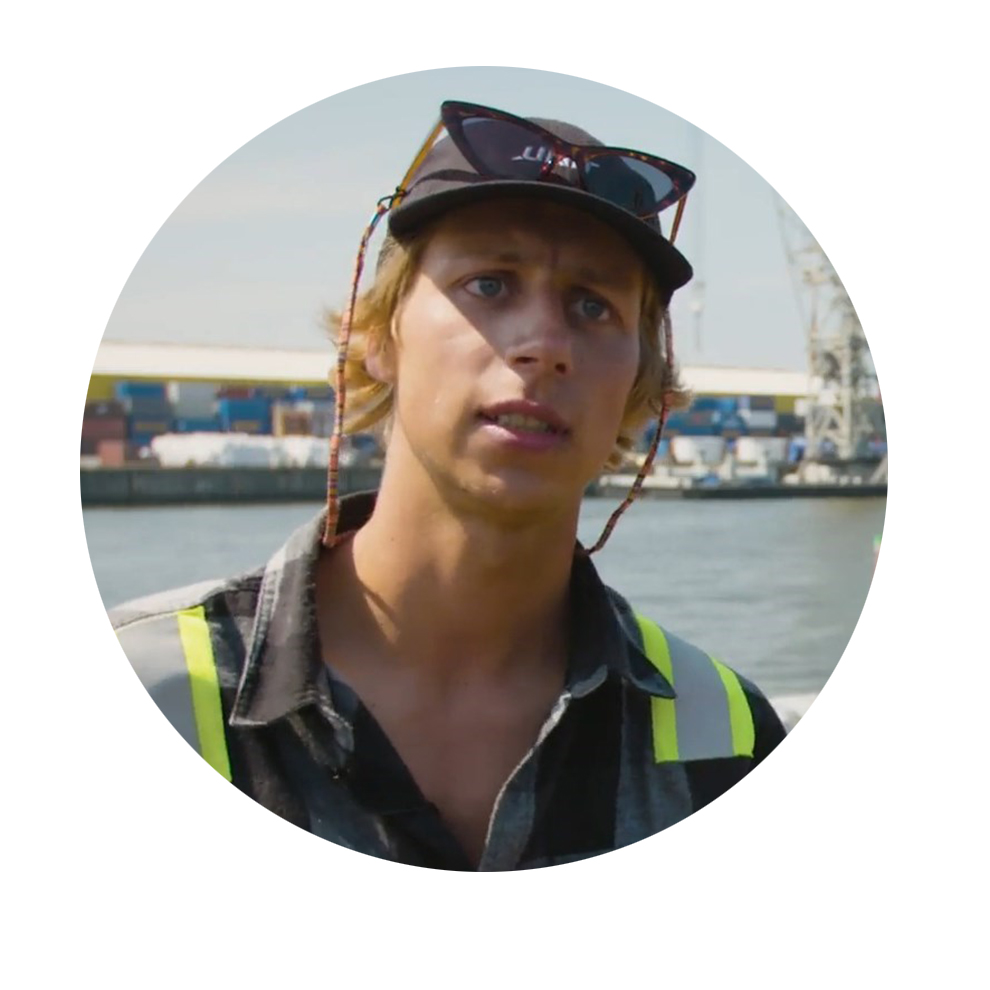A young man with blonde hair is wearing a safety vest at the harbor.