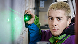 A young man with blonde hair is using a green laser on a wall.