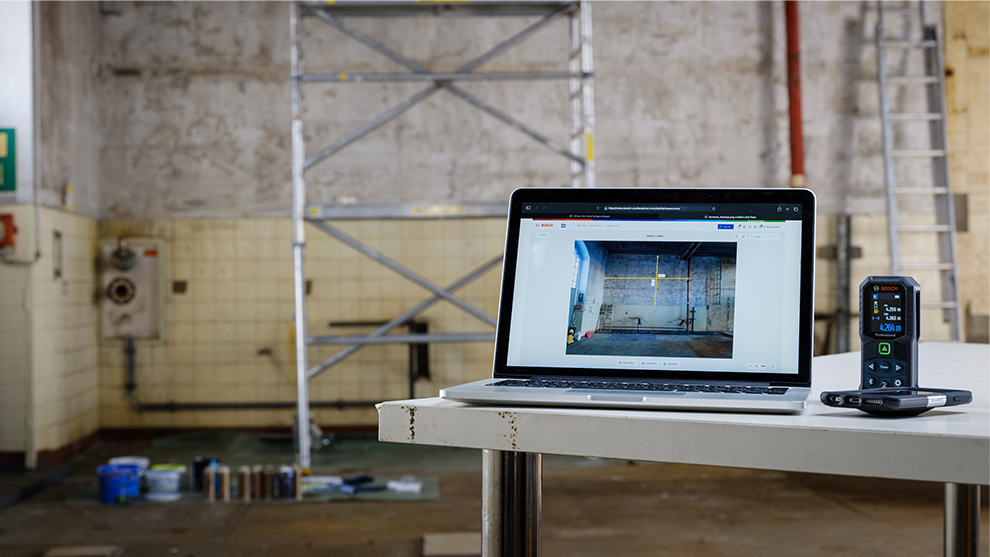 A laptop and a laser distance meter are on a table.