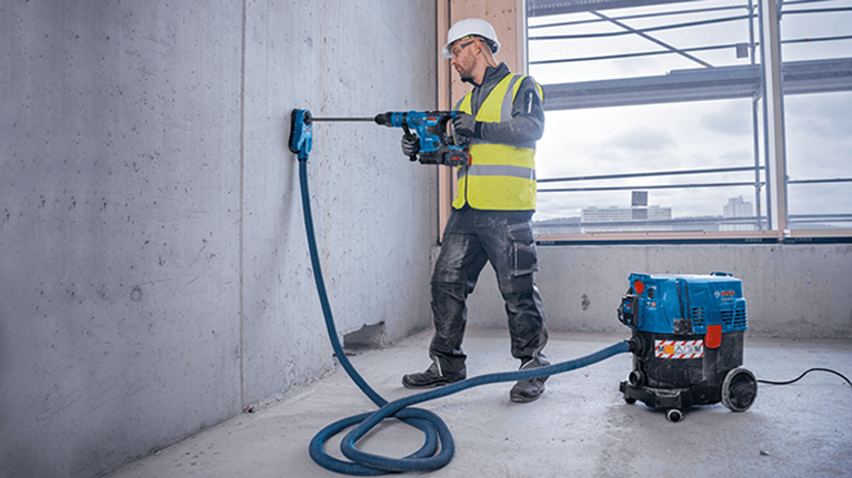 A craftsman with a drill is working on a wall in a construction site.