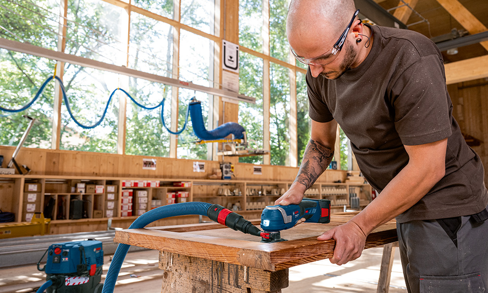 Sanding a door with a multi-cutter A craftsman is using a blue Bosch battery sander in a workshop.