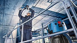 A worker in blue clothing is using a Bosch tool at a construction site.