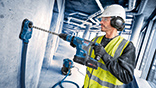 Worker with helmet and safety vest drilling into a wall with a Bosch tool.