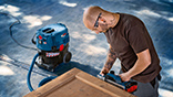 A man is working with a blue Bosch Professional battery nailer on wood.