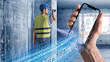 A worker in a yellow vest is using a smartphone in a room.