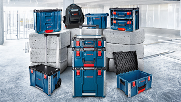 Various blue Bosch Professional tools and cases are placed on gray concrete blocks in a bright environment.