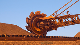 An orange bucket-wheel excavator is transferring material onto a conveyor belt.