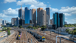 Train lines lead to modern skyscrapers under a blue sky.