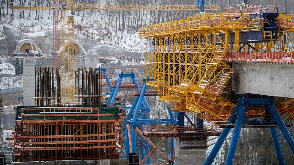 Yellow and blue scaffolding at a construction site in the snow with cranes.