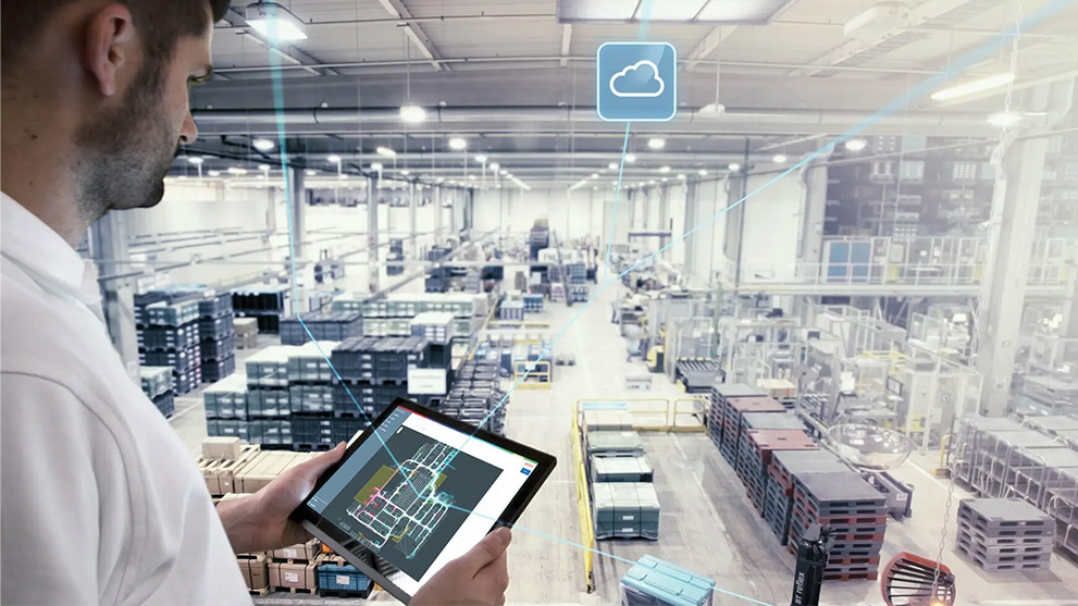 A man is looking at a tablet screen in a large factory hall.