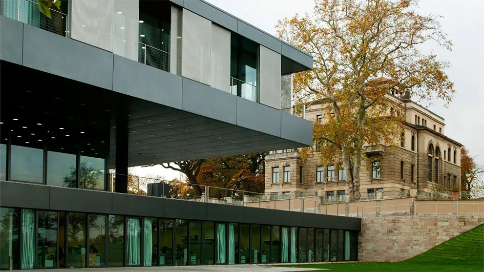 Modern gray architecture with glass facade and historic building in the background.