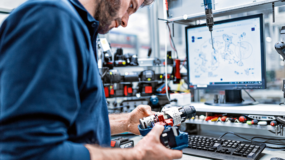 A man checks a Bosch Professional tool on a table with a monitor.