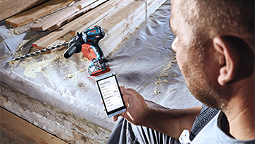 A man with a smartphone is looking at a Bosch Professional machine.