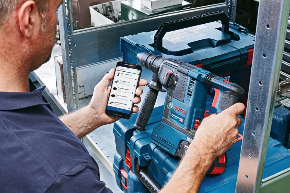 Man holds Bosch Professional rotary hammer and smartphone in the workshop.