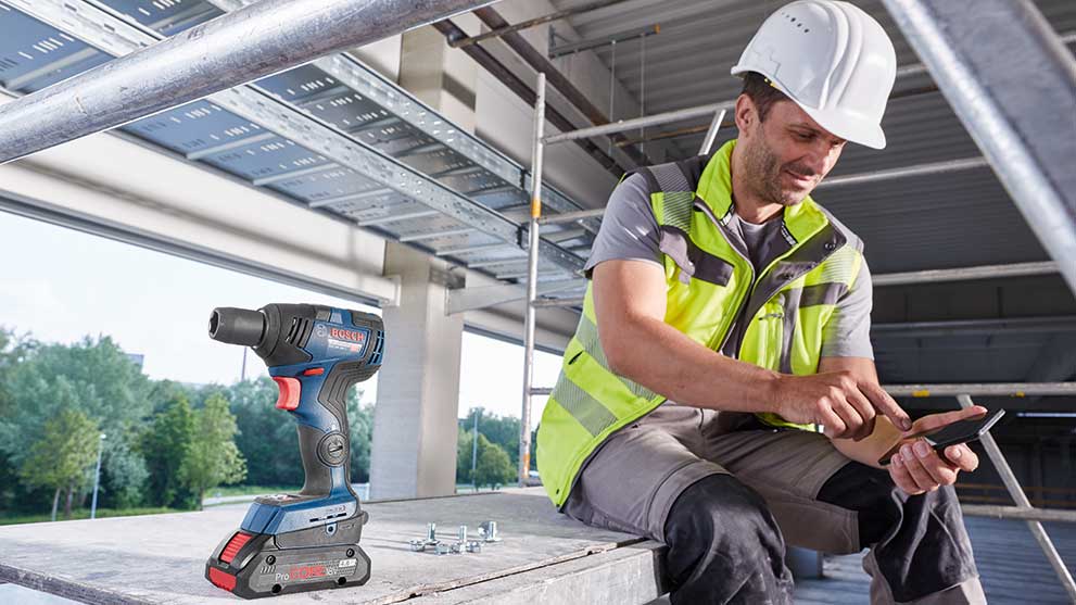 A Bosch Professional cordless screwdriver stands next to a construction worker with a phone.
