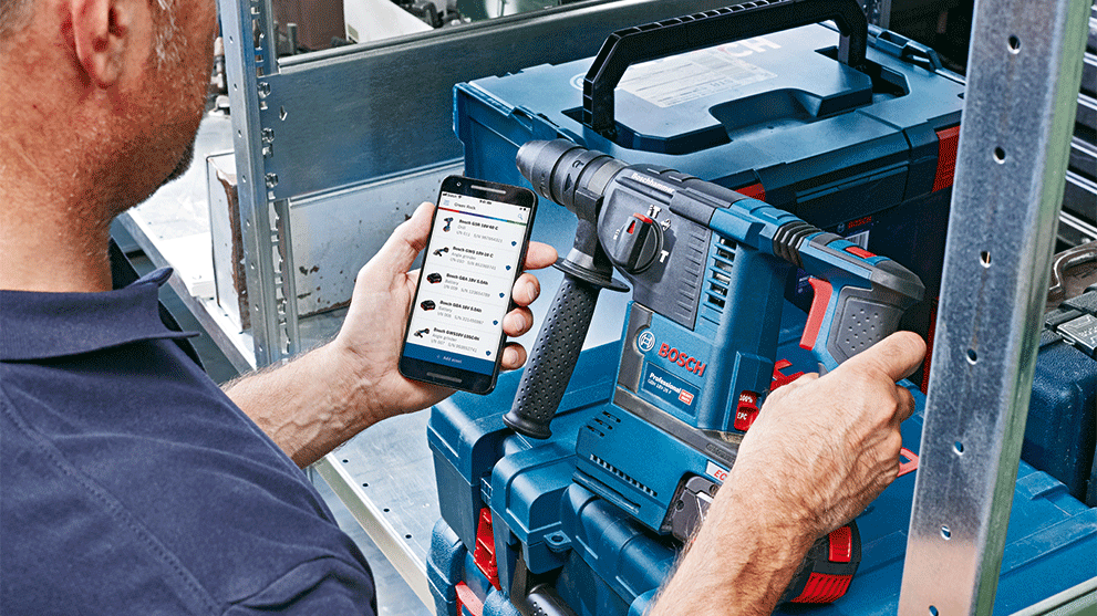 A man holds a smartphone and a Bosch Professional drill.