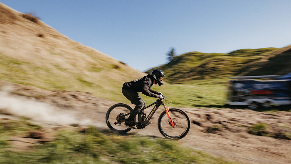 A mountain biker rides quickly down a slope, dust swirling up.