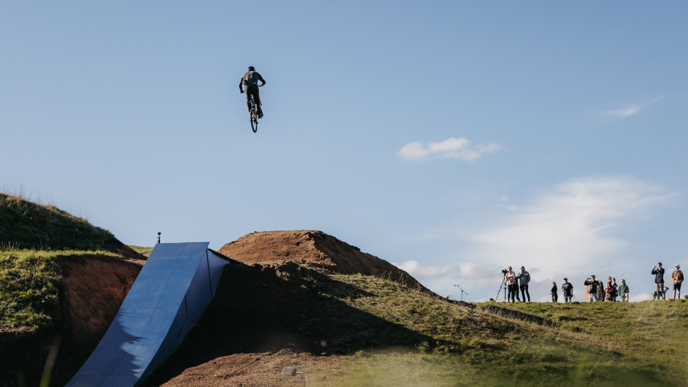 A BMX rider jumps over a blue ramp in front of an outdoor audience.