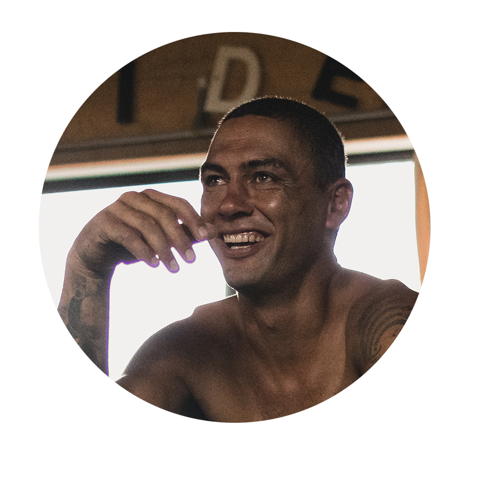 A smiling man with tattoos is sitting in a bright room.