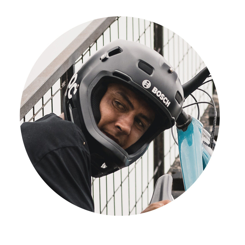 A man with a black Bosch helmet looks at the camera, holding a bicycle.