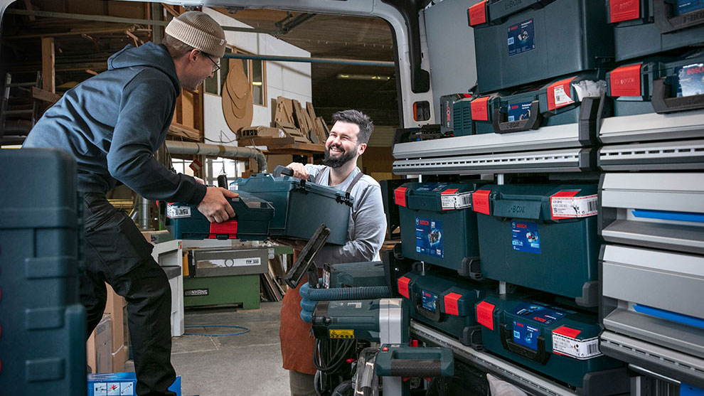 Two men are loading a Bosch Professional tool case into a van.