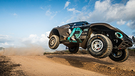 A black off-road racing car jumps over a sandy track.