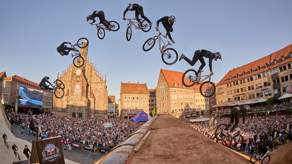 A track builder drills into wood on top of the tallest slope in Nuremberg's main square  A BMX rider jumps over a ramp in front of a large crowd.