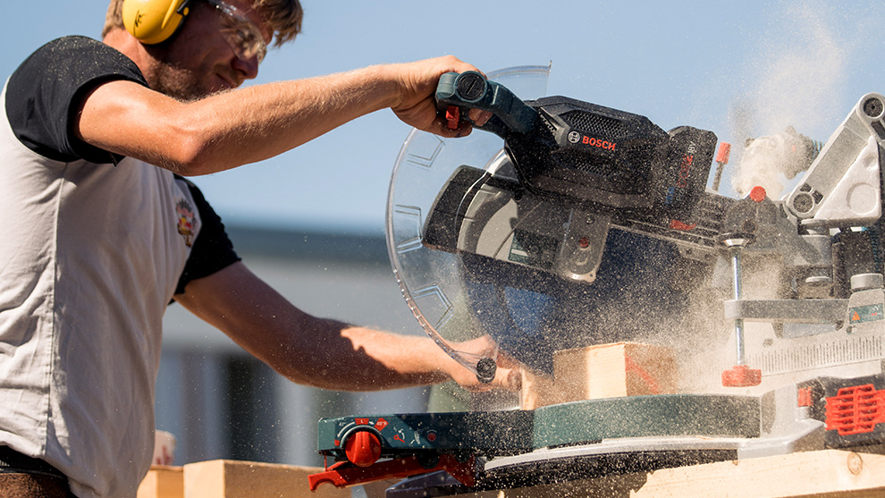 The team used the portable BITURBO mitre saw GCM 18V-305 GDC for fast and powerful wood-cutting A man wearing hearing protection is cutting wood with a Bosch Professional miter saw.