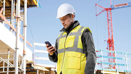 A construction worker in a yellow vest and helmet is looking at his smartphone.