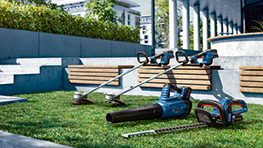 Three Bosch Professional tools lie on green grass, surrounded by benches.